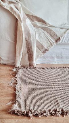 Manta de algodón con rayas marrones, colocada sobre un sofá blanco, junto a una alfombra de textura similar.