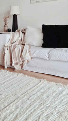 Manta de algodón con rayas marrones sobre un sofá blanco, decorando un ambiente acogedor.