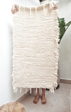 Alfombra lisa de algodón de 110x60 cm, sostenida por una persona, mostrando su textura suave y color claro.