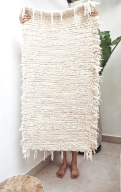 Alfombra lisa de algodón de 110x60 cm, sostenida por una persona, mostrando su textura suave y color claro.