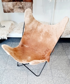 Sillón BKF de cuero de vaca en color marrón claro, con estructura metálica negra, ubicado en un ambiente decorativo.