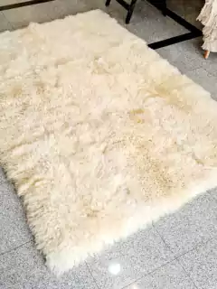 Alfombra de cuero de oveja Sarakina, color crema, con textura suave y peluda, de 120x180 cm, sobre un suelo de baldosas.