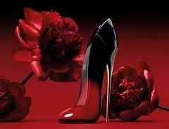 Frasco do perfume Very Good Girl Elixir Carolina Herrera em formato de sapato de salto alto vermelho e preto, com flores vermelhas ao fundo