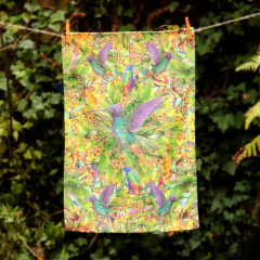 Toalla pequeña de microfibra con diseño de colibríes sobre un fondo de hojas y flores coloridas.