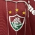 Detalhe do escudo da Camisa Fluminense III Retrô 2007/2008, com cores grená e branca e três estrelas acima do escudo.