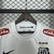 Camiseta retrô branca do Santos FC, com detalhes em preto e logos de patrocinadores, pendurada em um cabide.