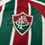 Detalhe do escudo da camisa feminina Fluminense 2025/2026, com as cores verde e grená e listras verticais.