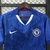 Camisa de futebol do Chelsea na cor azul e branca, com detalhes em azul e logo do clube na parte frontal.