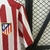 Camisa branca e vermelha do Atlético de Madrid, com detalhes em vermelho e escudo do time na parte superior esquerda.