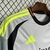 Camisa do Benfica III 2024/2025 nas cores cinza e preta, com detalhes em amarelo, pendurada em uma grade.