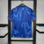 Camisa de futebol azul com padrão fluido nas costas, pendurada em um suporte. Detalhes em laranja nas mangas.