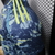 Camisa do Ajax II 24/25 da Adidas, em azul marinho com detalhes em verde azulado, vista lateral destacando os ombros e as listras amarelas.