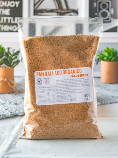 Paquete de pan rallado integral orgánico Hausbrot de 500g sobre una mesa, con etiqueta visible que detalla la información nutricional.
