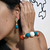 Conjunto de pulseira e brinco banhado dourado com esferas grandes nas cores azul, branco e laranja, usado por mulher. Acessórios da Coleção Nova Outono-Inverno 2026.
