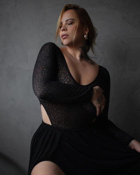 Mulher usando body preto de manga longa em rendão com cava alta, com detalhes em renda e saia preta