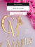 Letreiro de acrílico dourado personalizado com as letras CM e borboleta decorativa, fixado em parede rosa com flores cor-de-rosa ao redor.