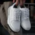 Zapatillas blancas de cuero modelo Trust One, sostenidas por una mano.