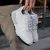 Tenis blancos modelo Trust One, sostenidos por una mano, con detalles en negro en la suela.