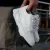 Par de zapatillas blancas de diseño moderno, sostenidas por una mano, con detalles en negro en la suela.