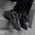 Un par de zapatillas deportivas negras con detalles en malla, colocadas sobre una superficie de piedra.