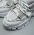 Primer plano de zapatillas Aglet de color blanco con detalles en gris y cordones trenzados.