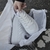 Un par de zapatillas deportivas blancas recién sacadas de su caja, sostenidas por una mano. Las zapatillas están sobre papel de seda dentro de la caja.