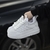 Un par de zapatillas deportivas blancas con suela gruesa, sostenidas por una mano, frente a un auto.