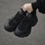 Un par de zapatillas negras con detalles en malla, sostenidas con una mano sobre un fondo gris.