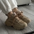 Vista cercana de zapatillas deportivas en tonos beige, con detalles de malla y suela gruesa, usadas con pantalones blancos.