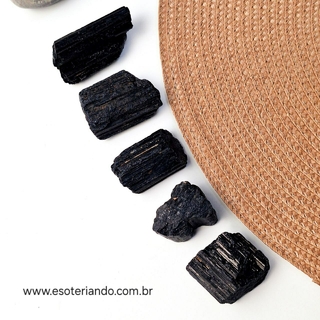 Quatro pedras de turmalina negra bruta na palma da mão, variando em tamanhos e texturas.