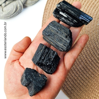 Quatro pedras de turmalina negra bruta na palma da mão, variando em tamanhos e texturas.