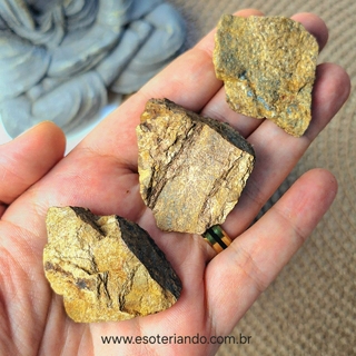 Pedras brutas de bronzita em um recipiente de barro, apresentando diversas formas e texturas.