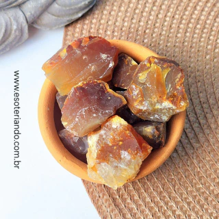 Pedaços de cornalina bruta em um recipiente de barro, com tons avermelhados e dourados.