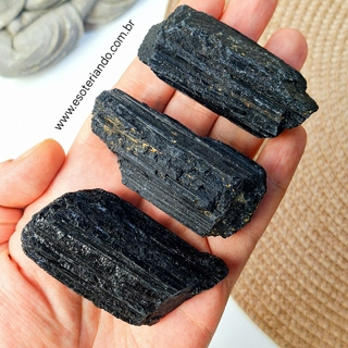 Três pedras de turmalina negra bruta, variando em tamanho, exibidas na palma da mão.