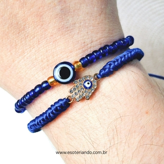 Conjunto de pulseiras com design de olho grego, incluindo contas azuis e um pingente em forma de mão, apresentado em um cartão informativo.