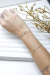 Bracelete De Prata Valerie minimalista em prata 925 no pulso de uma pessoa, com detalhes de tatuagens visíveis e fundo branco decorativo.