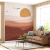 Papel de parede Boho com um pôr do sol no deserto, apresentando ondas em tons de terracota e um sofá na sala de estar.