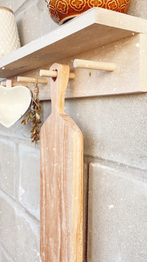 Estante perchero de madera con utensilios de cocina y decoración sobre una pared de ladrillos grises.