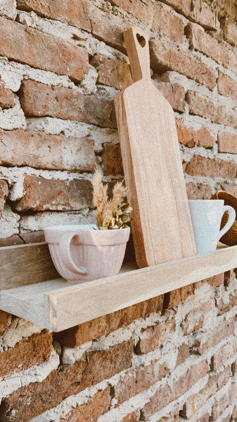 Estante Calipso Petiribi con tazas y una tabla de madera sobre una pared de ladrillos expuestos.