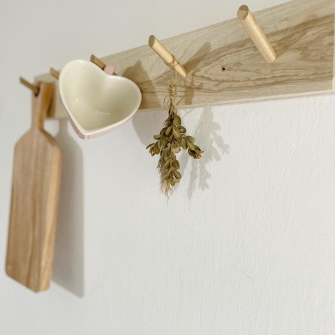 Perchero Arrayán Petiribi con una taza en forma de corazón, una rama de hojas secas y una tabla de madera colgando.