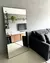 Espelho de chão retangular encostado na parede de uma sala moderna com sofá escuro e decoração minimalista.
