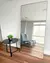 Espelho de chão Light com moldura básica em ambiente moderno, ao lado de uma mesa preta com planta decorativa.
