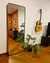Espelho de Chão Square em uma sala com decoração moderna, incluindo uma guitarra na parede e planta no chão.