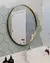 Espelho redondo Moon com moldura dourada instalado em banheiro moderno, acima de pia branca e parede com azulejos hexagonais.