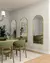Espelhos de pendurar Moonlight com moldura dourada em parede de sala de jantar moderna, destacando cadeiras verdes e decoração sofisticada.