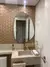 Banheiro moderno com espelho orgânico sem moldura, parede decorada com revestimento hexagonal bege e bancada de mármore com acessórios dourados.