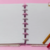 Caderno Diskô Gran Rosa pequeno com folhas em branco e disco rosa, ao lado de canetas coloridas.