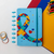 Caderno Diskô Amor ao Autista com capa azul e detalhes coloridos em formato de quebra-cabeça.
