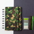 Caderno Diskô Classic Camuflado com capa em camuflagem e folhas em branco, acompanhado de canetas e uma paleta de cores.