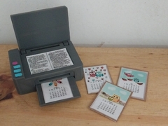 Impresora miniatura articulada para casita de muñecas con impresiones de calendarios coloridos.